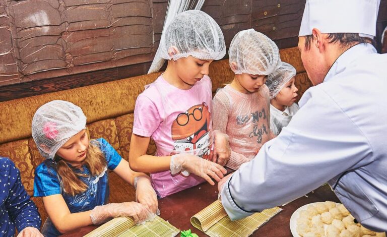 A group of children learning to cook sushi under a chef's guidance.